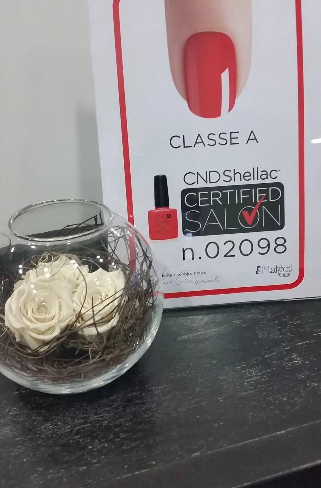 Targa CND Shellac Certified Salon di Classe A accanto a una rosa bianca