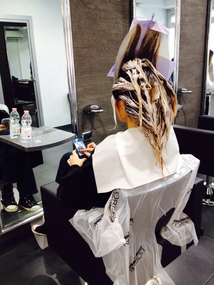 Una cliente con lo shatush in posa davanti agli specchi del salone, pareti in pietra grigia